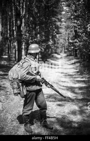 Unidentified ri-enactor vestito come soldato tedesco con un fucile permanente sulla strada nel bosco. I colori nero e bianco Foto Stock