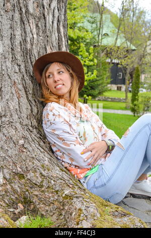 Ragazza appoggiata contro un albero nel parco Foto Stock