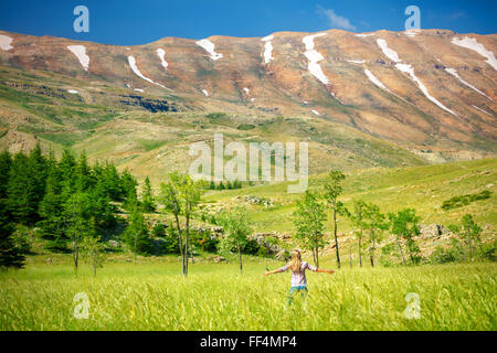 Felice donna in piedi con le mani alzate nella fresca valle verde vicino alle montagne, godendo della splendida natura del Libano Foto Stock