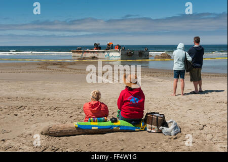 Turisti guarda i lavoratori rimuovere un cemento floating boat dock che era andato alla deriva in tutto il Pacifico dallo tsunami giapponese Foto Stock