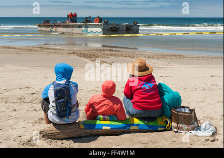 Turisti guarda i lavoratori rimuovere un cemento floating boat dock che era andato alla deriva in tutto il Pacifico dallo tsunami giapponese Foto Stock