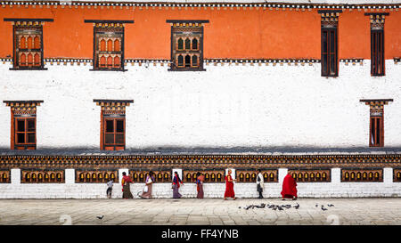 I fedeli e i monaci bhutanesi camminano lungo una lunga fila di ruote di preghiera accanto al muro esterno di Thimphu Dzong in Bhutan Foto Stock