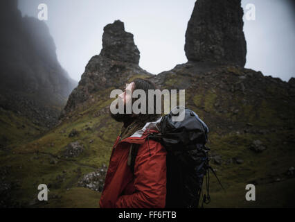 Un uomo in piedi con uno sfondo di pinnacoli di roccia sul torreggiante skyline su di lui, un cielo nuvoloso con bassa cloud. Foto Stock