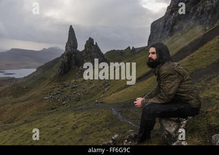 Un uomo seduto su una roccia con uno sfondo di pinnacoli di roccia sullo skyline, un drammatico paesaggio spazzate dal vento. Foto Stock