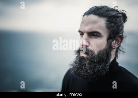 Un uomo con il pieno di barba e baffi e capelli neri rottamato indietro dal suo volto. Foto Stock