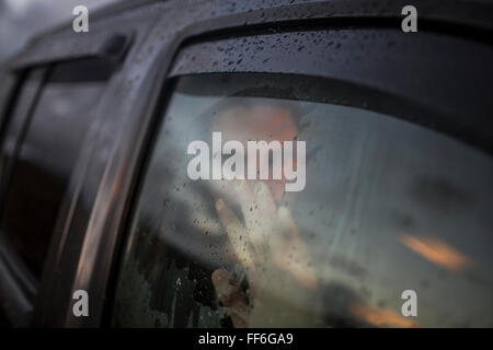 Un uomo seduto in un auto guardando fuori. Riflessioni del Cielo di tramonto sulla finestra. Foto Stock