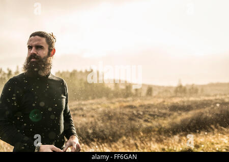 Un uomo in piedi nel soleggiato paese aperto d'inverno. Foto Stock