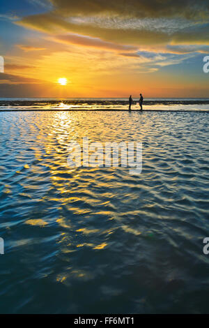 Due persone stagliano contro un tramonto riflesso in acqua Foto Stock