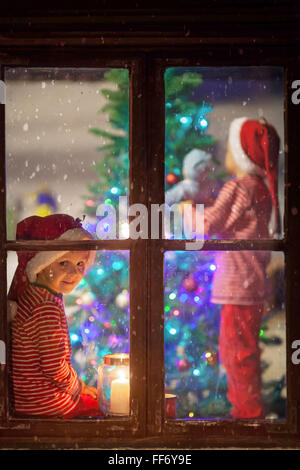 Dolce bambini, decorazione albero di natale, attesa con impazienza per Santa Claus, inverno nevica, bambino seduto su una finestra sh Foto Stock