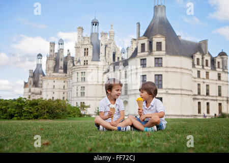 Due ragazzi adorabili in abbigliamento casual, mangiare il gelato seduto su un prato di fronte al più grande castello lungo il fiume Loira, C Foto Stock