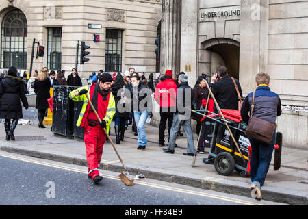 Un British street cleaner spazza la strada per pulire e rifiuti raccolti tra i molti pendolari presso la banca occupato incrocio nel centro di Londra, Regno Unito. La strada di servizio di pulizia è fornito da la City of London Corporation che è municipale il corpo direttivo. Foto Stock