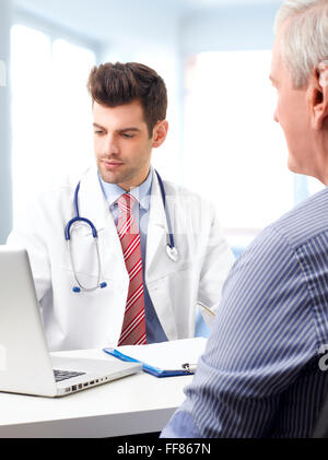 Bel giovane medico consultato con paziente anziano mentre è seduto alla scrivania nella parte anteriore del computer. Foto Stock