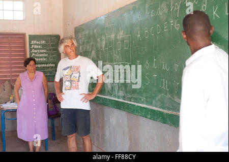 Mali, Africa - il giovane uomo nero si traduce la spiegazione matematica di due insegnanti caucasica insegnamento ai bambini neri in una tipica classe vicino a Bamako Foto Stock