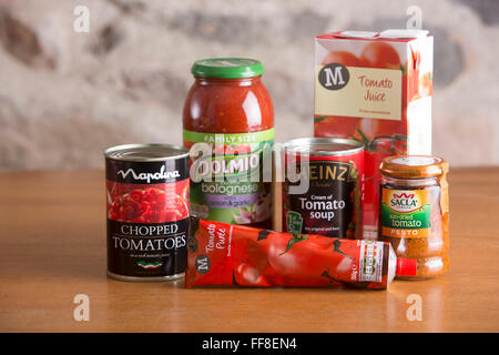 Selezione di conserve di prodotti a base di pomodoro compresi zuppa, succo, salsa, purè e conserve di tutti seduti su un paese tavolo da cucina Foto Stock