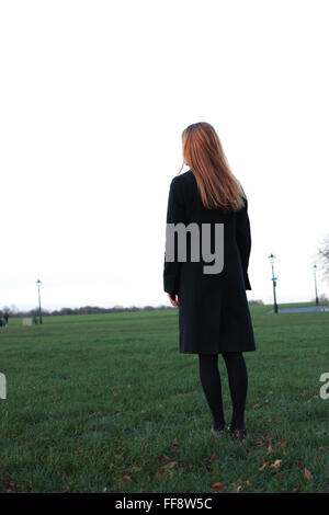 Malinconici giovane donna in piedi in un parco guardando in lontananza. Foto Stock