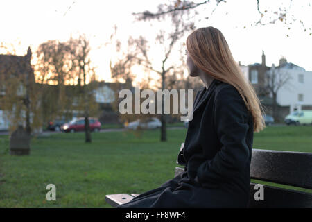 Giovani pensieroso donna seduta su una panchina guardando in lontananza. Foto Stock