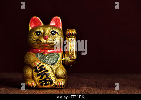 Un cinese golden lucky cat con la sua zampa sinistra sollevata su un rustico di una superficie di legno Foto Stock
