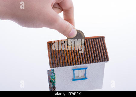 Mano moneta caduta nel salvadanaio a forma di un modello di casa Foto Stock