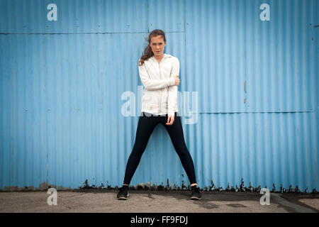 Donna in piedi da un blu ferro corrugato parete di indossare abbigliamento sportivo Foto Stock
