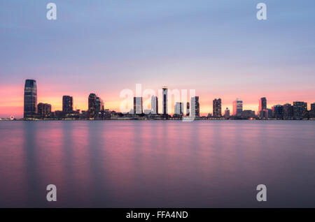 Un bellissimo tramonto sui grattacieli di Jersey City e il fiume Hudson, con il cielo rosa riflessa nell'acqua. Foto Stock