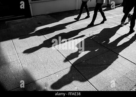 Ombra di quattro piedi pedoni proiettata sul marciapiede Foto Stock