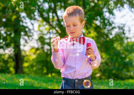 Un ragazzo in un parco verde di insufflazione di bolle di sapone Foto Stock