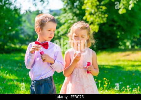 6 anno vecchio ragazzo guarda la ragazza rende le bolle di sapone Foto Stock