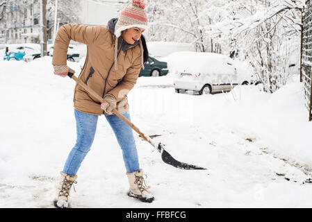 Donna felice spalare la neve nel parcheggio intorno a casa Foto Stock