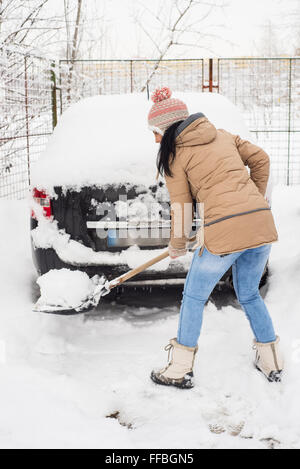 Donna di pulizia intorno neve auto e facendo un percorso Foto Stock