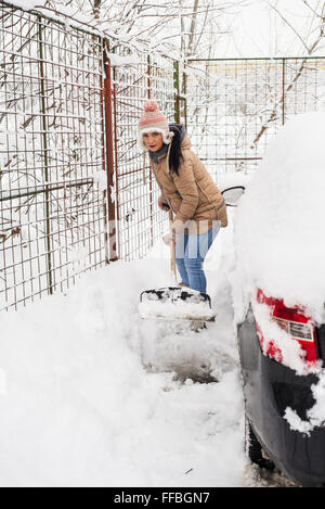 Donna spalare la neve intorno all auto in un freddo giorno Foto Stock