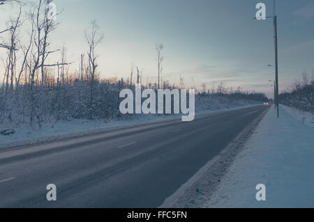 Strada rurale che conduce attraverso boschi innevati, tono vintage Foto Stock