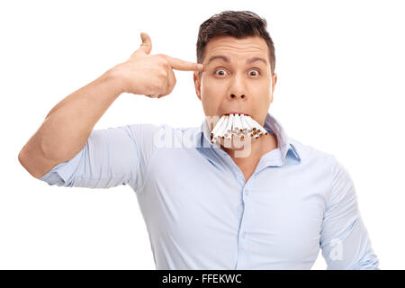 Studio shot di un uomo con un mazzo di sigarette nella sua bocca tenendo una mano la pistola contro la sua testa isolata su sfondo bianco Foto Stock