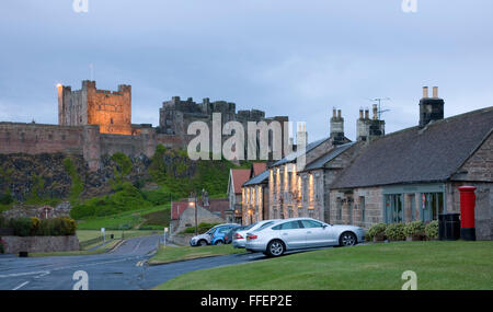 Bamburgh, Northumberland, Inghilterra. Vista lungo la strada per il mantenere illuminato di Bamburgh Castle, crepuscolo. Foto Stock