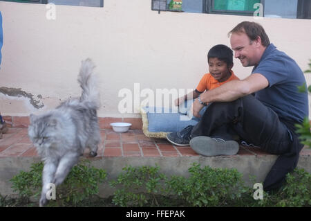 Cochabamba Bolivia. Caucasica padre matura per divertirsi con il suo latino adottato il ragazzo guardando un gatto al di fuori della loro casa Foto Stock