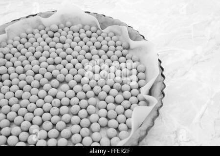 Close-up di pesi di pasticceria, ceramica semi in un grafico a torta crudi custodia foderata con carta da forno - elaborazione monocromatica Foto Stock