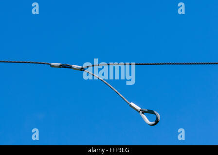 Unica sottile cavo metallico con un anello sospeso verso il basso contro il cielo blu e chiaro. Foto Stock