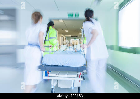 Moto fotografia sfocata del bambino il paziente sul lettino o di Gurney spinto a velocità attraverso il corridoio ospedaliero da parte di medici e infermieri Foto Stock