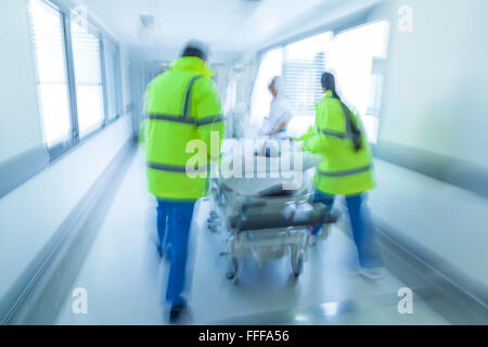 Moto fotografia sfocata del bambino il paziente sul lettino o di Gurney spinto a velocità attraverso il corridoio ospedaliero da parte di medici e infermieri Foto Stock