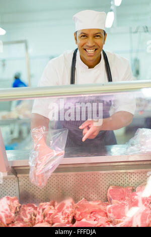 Allegro media età del macellaio di carne di puntamento in macelleria Foto Stock
