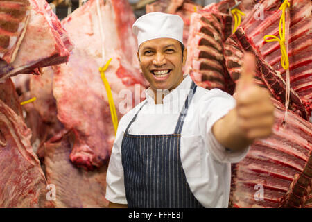 Allegro metà età butcher pollice in su in camera fredda Foto Stock