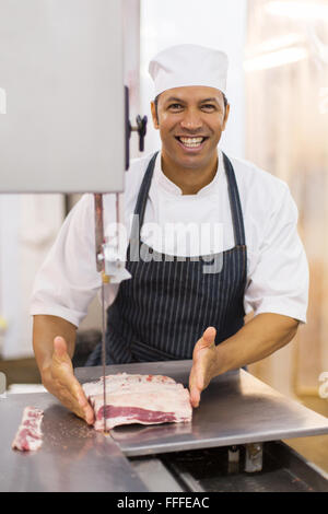 Ritratto di Allegro maschio maturo macellaio del taglio della carne sulla segatrice a nastro Foto Stock