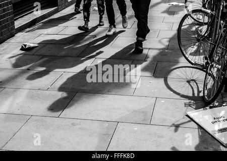 Ombre di tre piedi pedoni proiettata sul marciapiede con la bicicletta sul lato Foto Stock