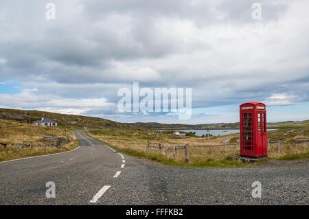 Svuotare strada di campagna nelle highlands scozzesi con un tradizionale britannico rosso telefono casella sul lato Foto Stock