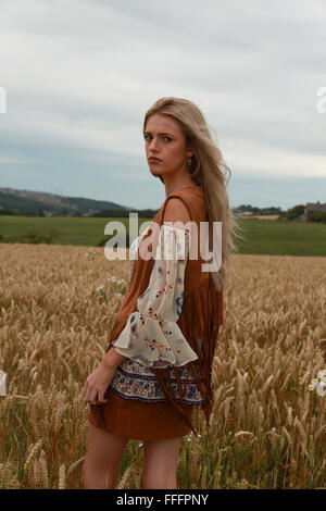 Bella ragazza seduta in un campo di grano guardando dritto alla telecamera con moody sky Foto Stock