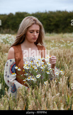 Bella ragazza in un campo di grano guardando alcune margherite Foto Stock