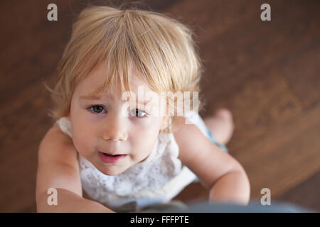 Ritratto di blonde caucasian baby due anni permanente e la ricerca di fotocamera gamba di contenimento che indossa un abito bianco o estate shirt Foto Stock