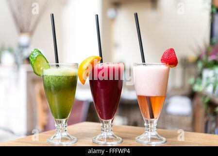 Tre Bicchieri di frutta e verdure fresche frullati disposti in una fila su un tavolo di legno Foto Stock