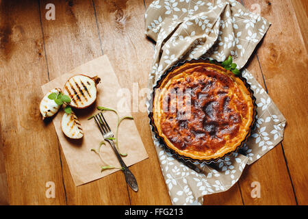 Torta di cipolle o Tart servita con grigliate di metà della cipolla e erbe aromatiche fresche su un tavolo di legno. Stile rustico. Vista dall'alto. Foto Stock