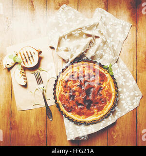 Torta di cipolle o Tart servita con grigliate di metà della cipolla e erbe aromatiche fresche su un tavolo di legno. Stile rustico. Vista dall'alto. Immagine con tonico Foto Stock