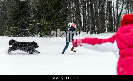 Due sorelle a giocare nella neve con il cane newfoundlander, inverno e tempo libero Foto Stock